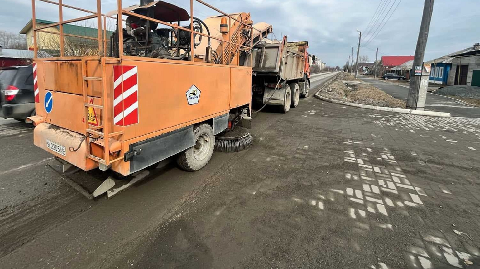 Специальная машина увлажняет дорогу и наваливает кучи мусора